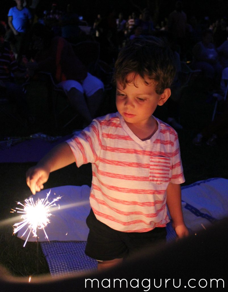 Boy in red and white striped shirt holds a sparkler on the 4th of July for summer fun